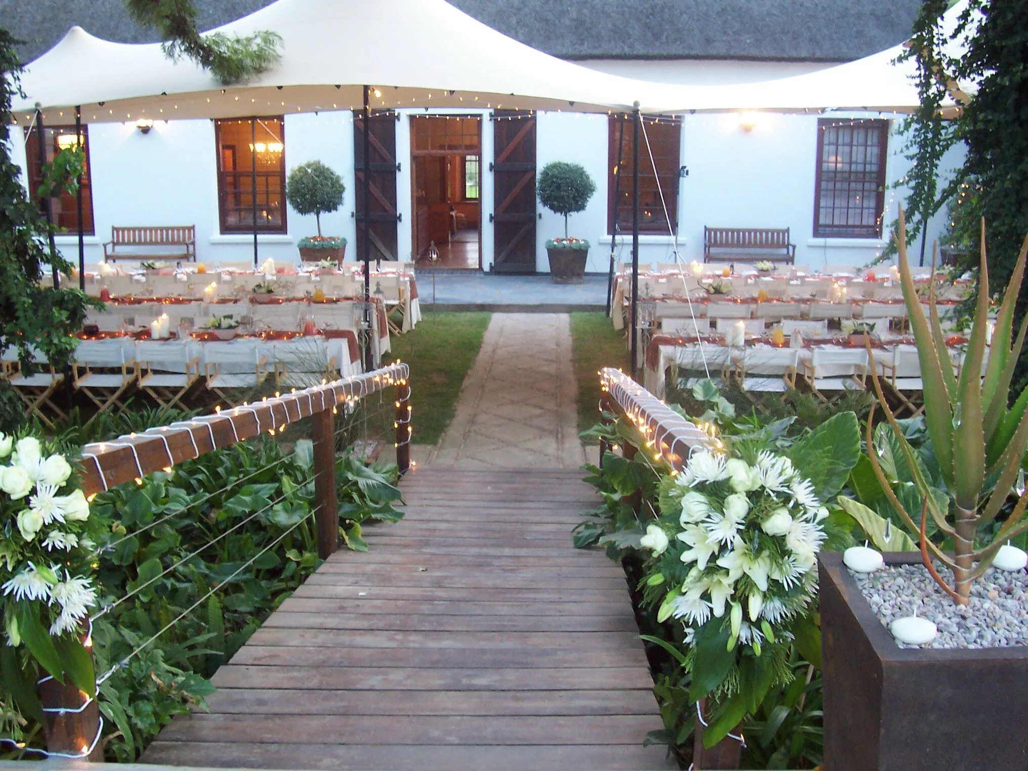 A boardwalk leading to a stretch tent in front of a farmhouse