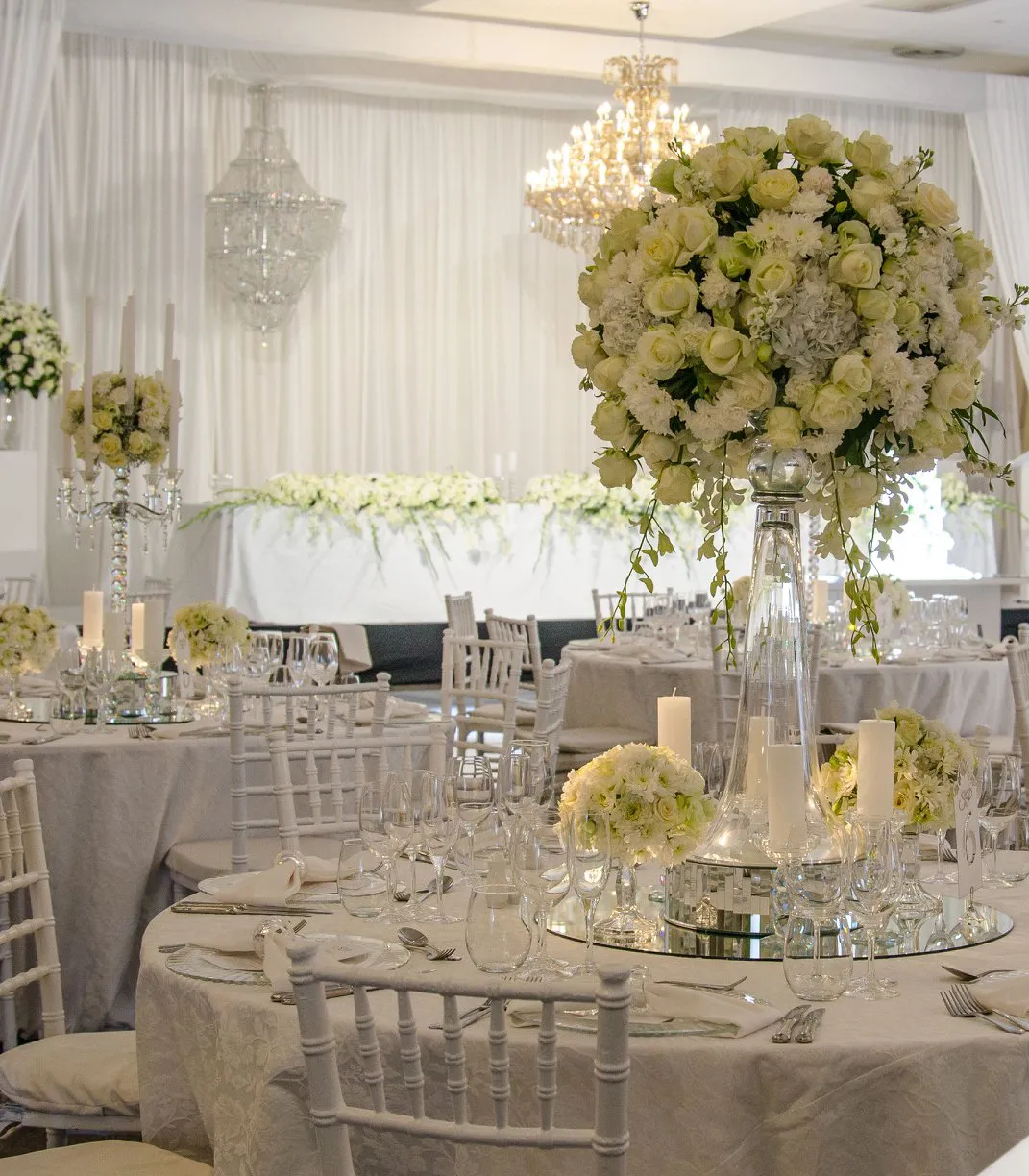 A draped room with chandeliers, white roses and round tables