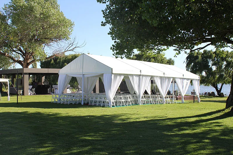 A white frame tent with tied-back curtains under trees