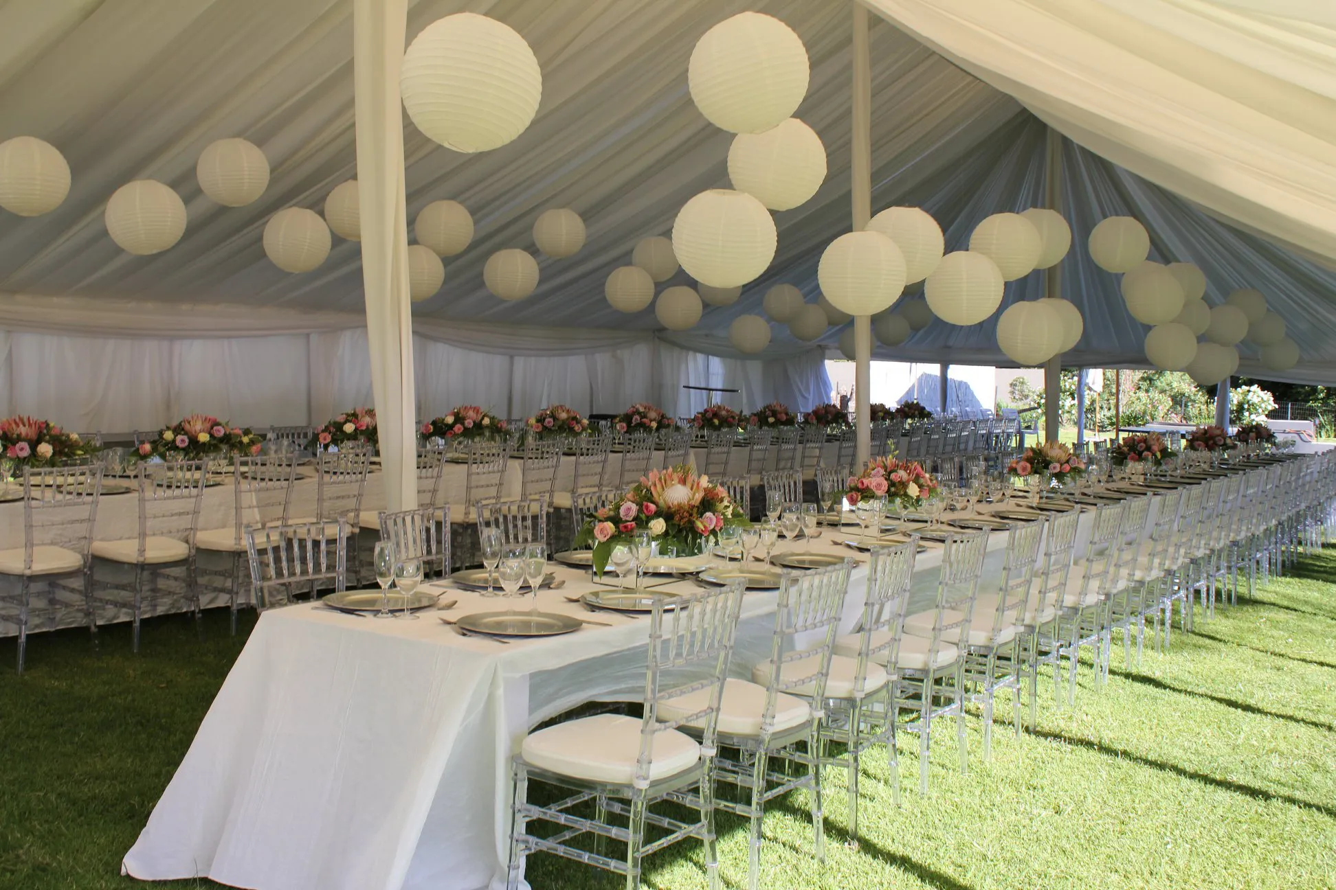 A draped marquee with white paper lanterns over long tables on the lawn