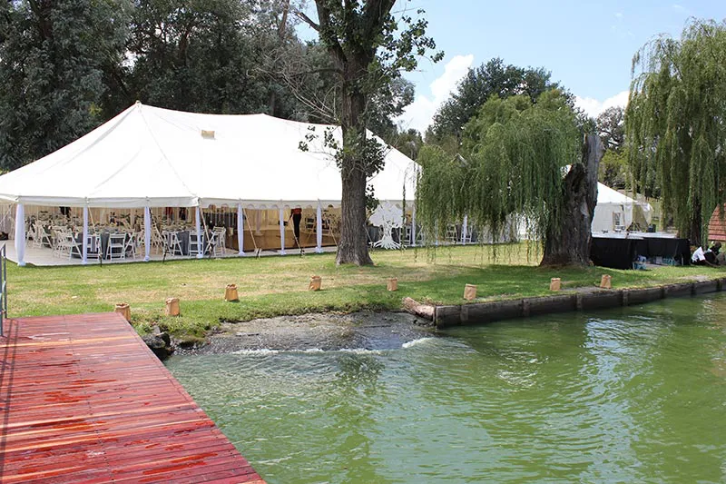 A peg and pole marquee beside a pond with a red boardwalk