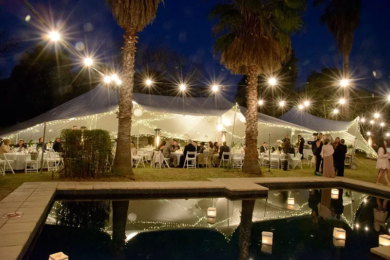 A stretch tent lit with festoon lights at night beside a pool