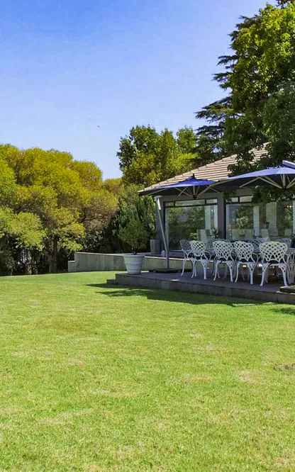 A garden with a covered terrace set with white chairs and umbrellas